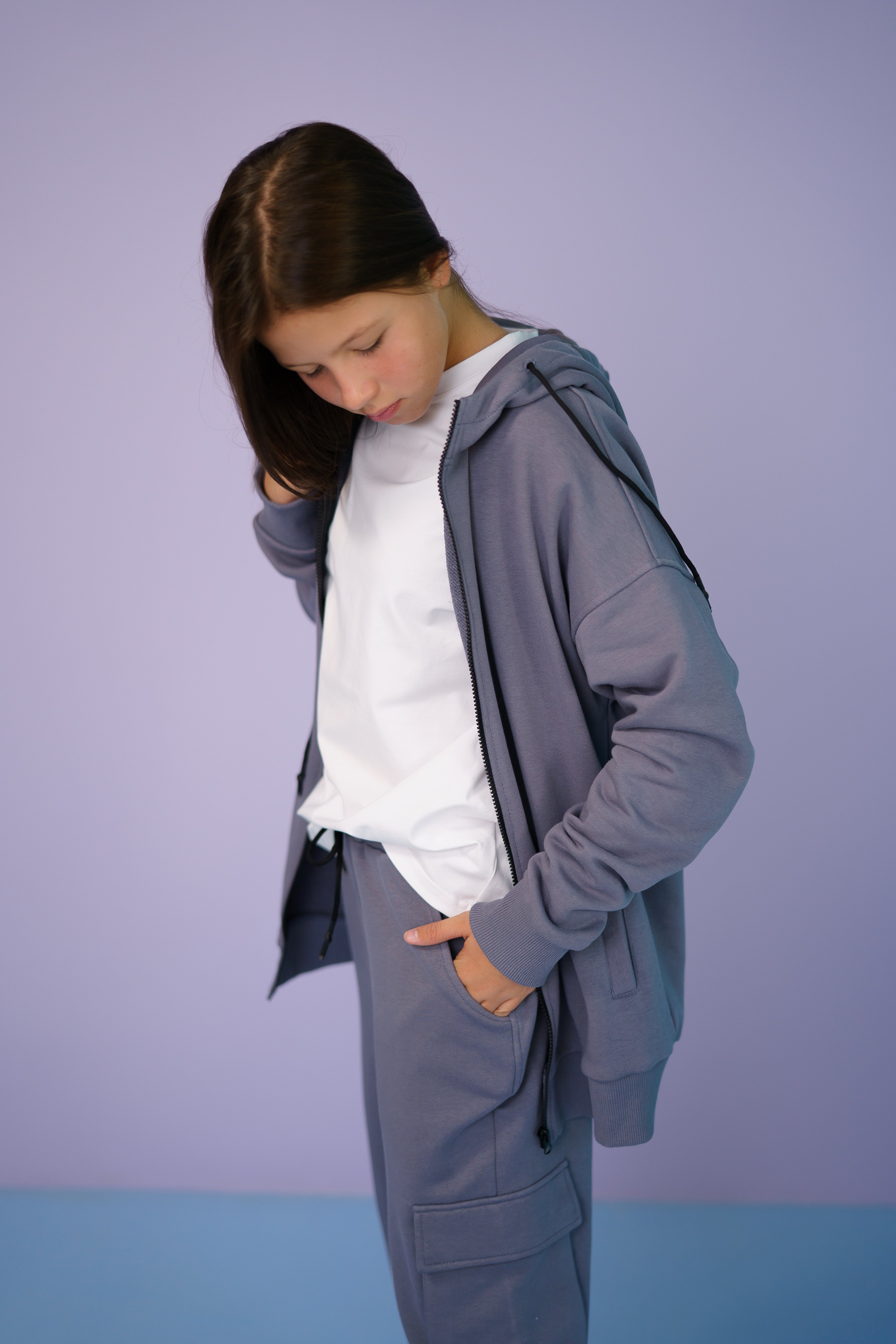 girl wearing a gray tracksuit and a white t-shirt looks to the ground