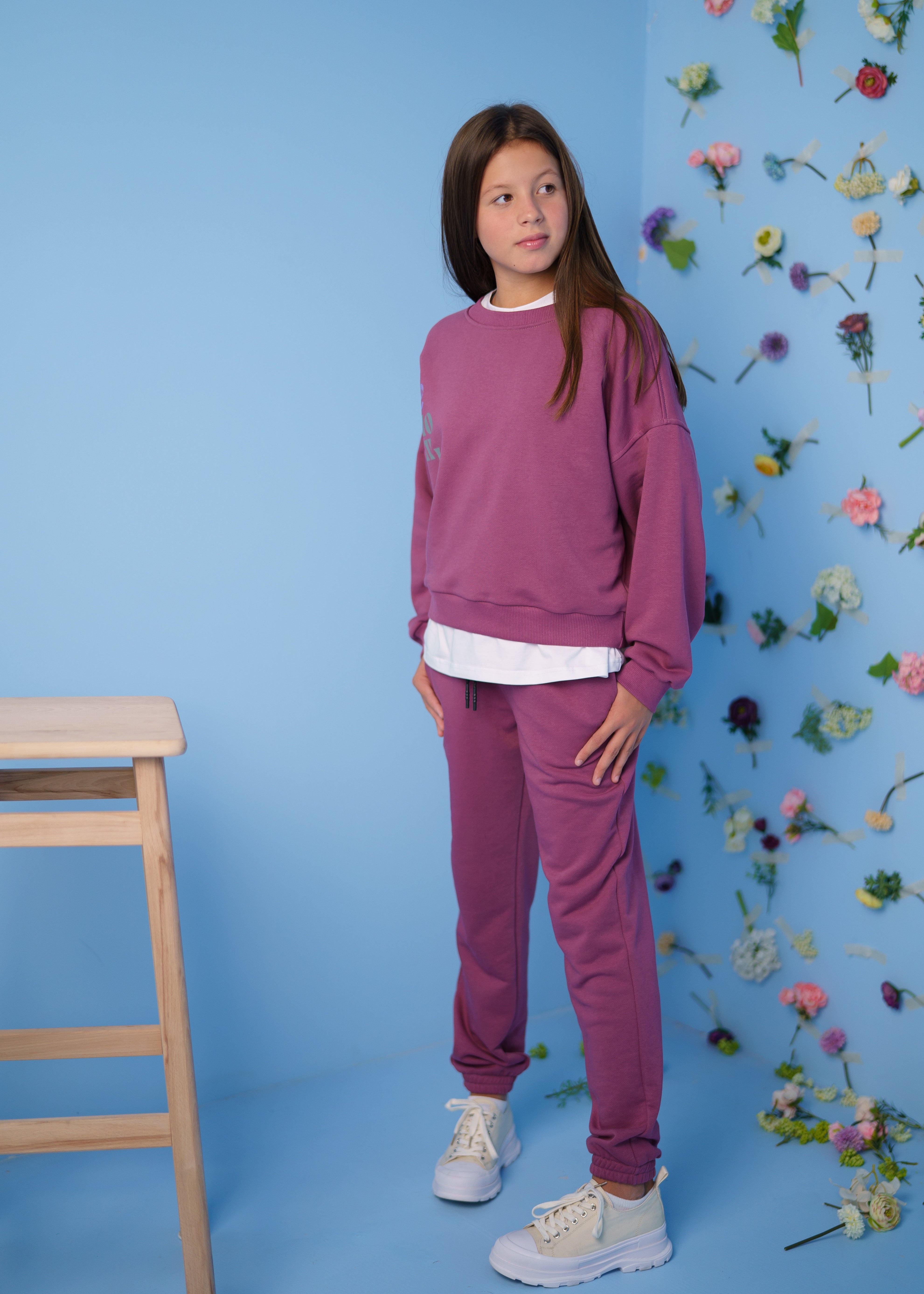 girl wearing a pink tracksuit with a sweatshirt by Lemoni  with a flower wall  on the background